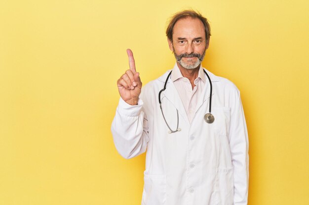 Médecin avec stéthoscope en studio jaune montrant le numéro un avec le doigt