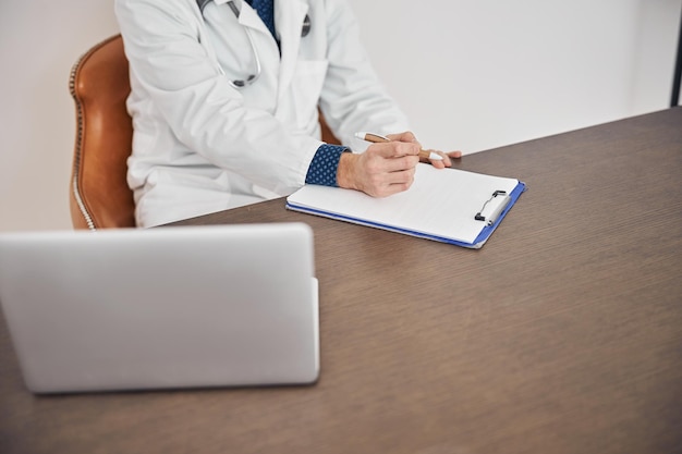 Médecin avec un stylo à la main assis au bureau