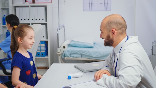 Médecin sympathique faisant un high five avec un enfant assis au bureau. Médecin de santé spécialiste en médecine fournissant des services de soins de santé examen de traitement radiographique dans le cabinet de l'hôpital