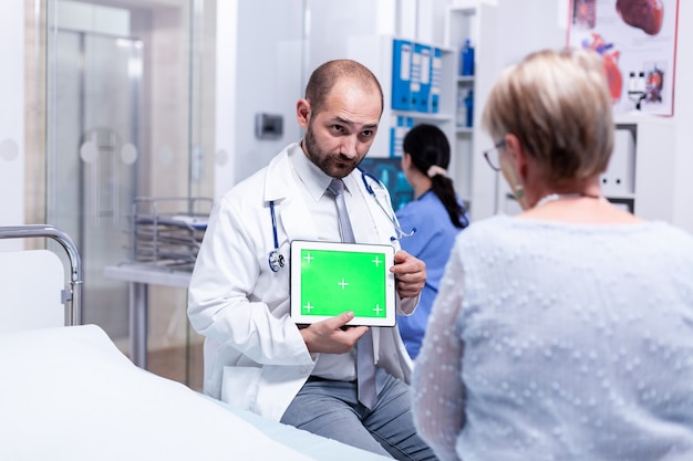 Médecin avec tablette à écran vert devant un patient âgé expliquant le diagnostic médical