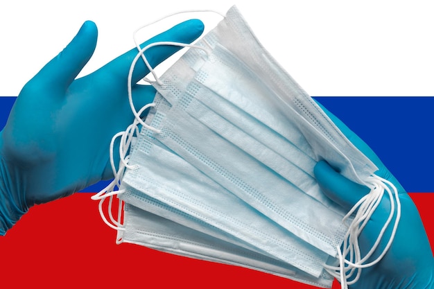 Médecin tenant des masques faciaux dans les mains des gants bleus chirurgicaux sur fond drapeau national de la Russie Concep...