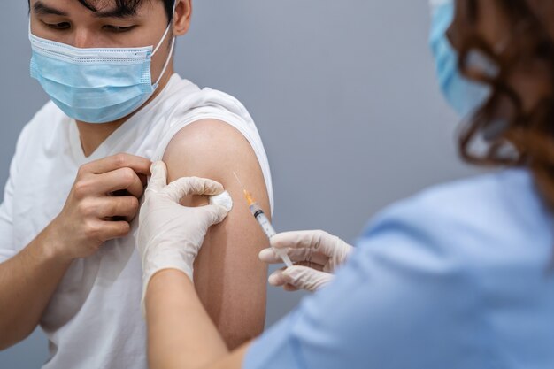 Médecin tenant la seringue et utilisant du coton avant de faire l'injection au patient dans un masque médical. Vaccin Covid-19 ou coronavirus