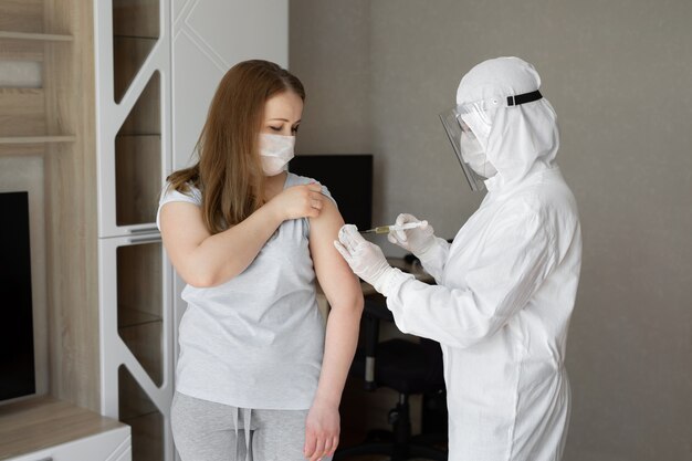 Médecin en tenue de protection individuelle ou EPI injecter le vaccin injecté pour stimuler l'immunité d'une patiente à risque d'infection par un coronavirus. Coronavirus, covid-19 et concept de vaccination