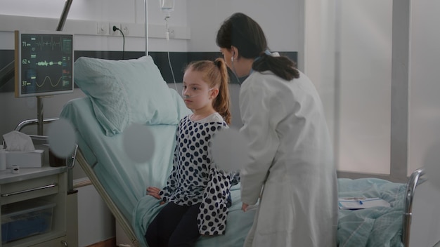 Médecin thérapeute consultant un enfant malade mettant un stéthoscope sur la poitrine du patient écoutant le rythme cardiaque dans la salle d'hôpital. Enfant hospitalisé avec tube nasal assis dans son lit en convalescence après une chirurgie médicale