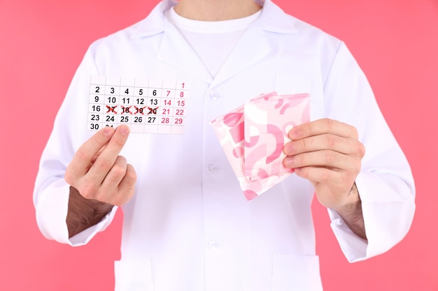 Le médecin tient le calendrier menstruel et les tampons sur fond rose