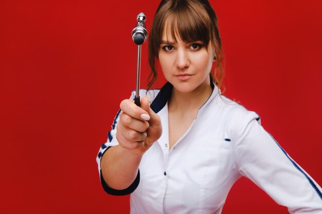 Le médecin tient un marteau neurologique sur fond rouge. Le neurologue vérifie les réflexes du patient avec un marteau. Diagnostic, soins de santé et soins médicaux