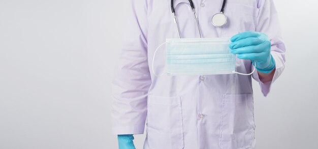 Le médecin tient un masque facial à la main avec des gants en latex bleus sur fond blanc