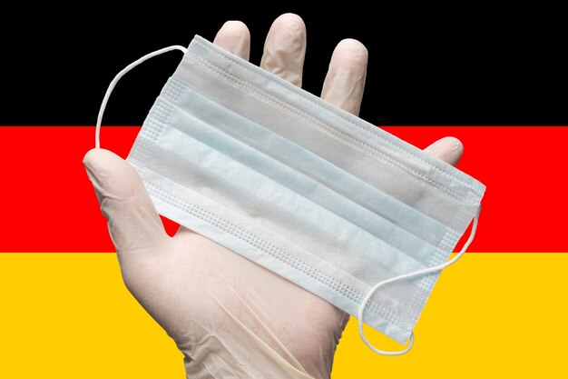 Le médecin tient un masque médical à la main dans des gants blancs sur le drapeau de couleurs de fond de l'Allemagne ou du drapeau allemand. Concept d'assurance pandémie coronavirus, grippe, quarantaine virale, épidémie pandémique, grippe.