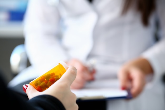 Une médecin tient un pot de pilules à la main.