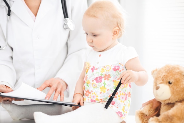 Médecin et tout-petit patient à l'hôpital. Une petite fille vêtue d'une robe à fleurs roses est examinée par un médecin avec un stéthoscope. Concept de médecine et de soins de santé.