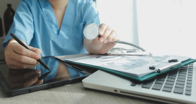 Médecin travaillant sur un ordinateur portable écrivant un presse-papiers de prescription avec des dossiers papier d'informations enregistrées sur le bureau de l'hôpital ou de la clinique Concept de soins de santé et médical Focus sur le stéthoscope