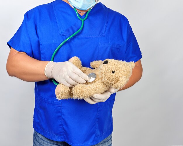 Médecin en uniforme bleu et gants en latex blanc tenant un ours en peluche brun