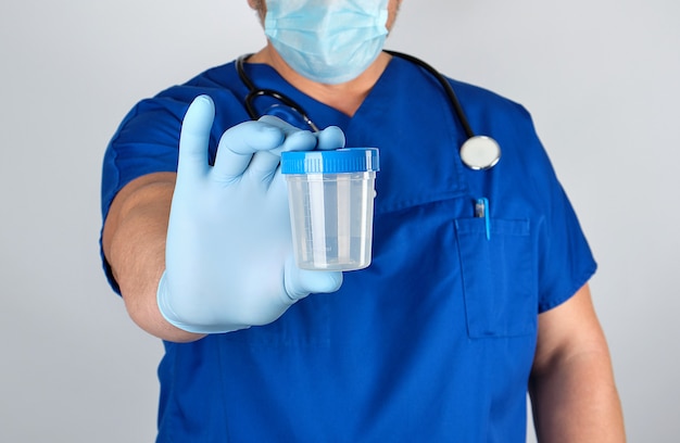 Médecin en uniforme bleu et gants en latex tenant un récipient en plastique vide pour prélever des échantillons d&#39;urine