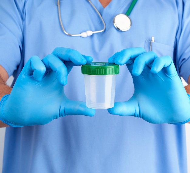 Médecin en uniforme bleu et gants en latex tenant un récipient en plastique vide pour prélever des échantillons d'urine