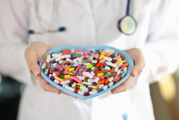 Un médecin en uniforme médical tient une assiette en forme de coeur avec des pilules colorées dans les mains diététiques