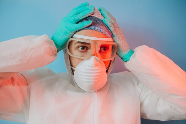 Médecin en uniforme de protection, masque respiratoire, lunettes, gants. Un portrait en gros plan d'un médecin en néon rouge. Un homme fatigué se bat contre un coronavirus. COVID 19