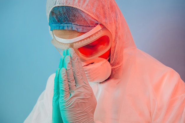 Médecin en uniforme de protection, réparateur, lunettes, gants. l'homme prie