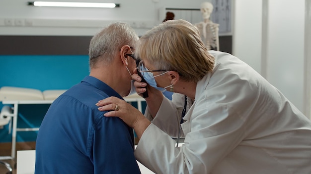 Médecin utilisant un otoscope pour faire un examen de l'oreille, consultant un vieux patient infecté pendant la pandémie de covid 19. Otologue examinant une personne avec un outil d'otologie lors d'une visite de contrôle médical.