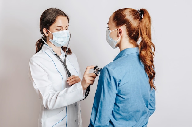 Médecin vérifiant la santé d'une patiente dans des masques avec un stéthoscope sur un fond blanc isolé