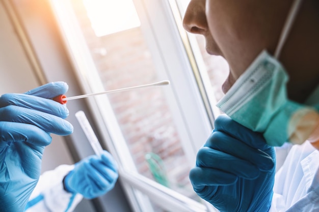 Un médecin en vêtements de protection prend un tube à essai sur écouvillon COVID19 de la bouche au centre de test Covid19 pendant le processus de protocole de test ADN PCR de l'épidémie de coronavirus