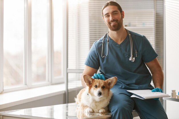 Médecin vétérinaire masculin réussi câlinant la tête d'un mignon chien corgi