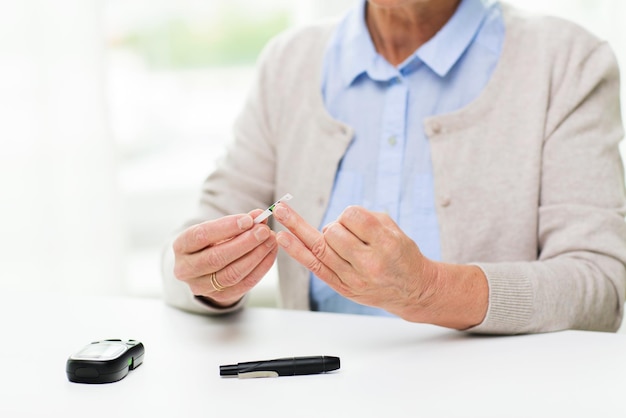 médecine, âge, diabète, soins de santé et concept humain - gros plan d'une femme âgée avec glucomètre vérifiant le taux de sucre dans le sang à la maison