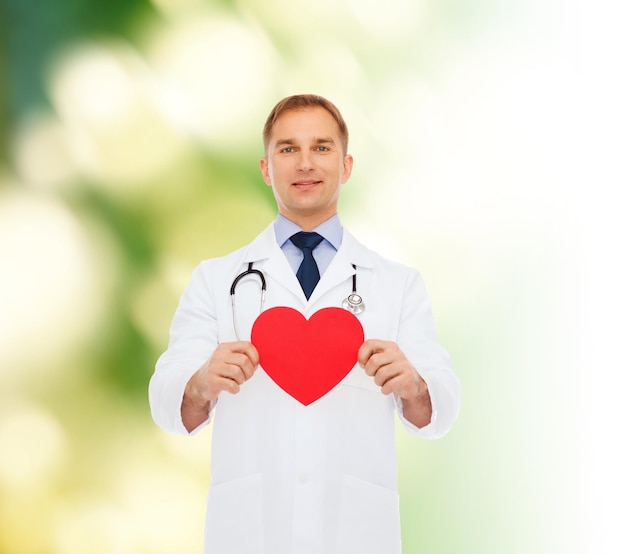 médecine, profession, charité et concept de soins de santé - médecin souriant avec coeur rouge et stéthoscope sur fond naturel