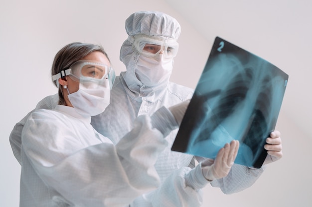 Les médecins debout sur fond blanc examinent les rayons X pour la pneumonie d'un patient Covid-19 à la clinique. Concept de coronavirus.