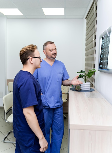 Les médecins examinent la radiographie d'un patient. Radiologues masculins debout près d'un tableau éclairé. Expérience en cabinet médical.