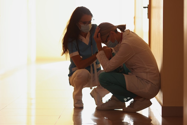 Médecins fatigués en masque médical de protection assis sur le couloir