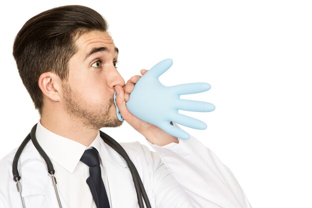 Les médecins s'amusent aussi! Prise de vue en studio d'un médecin de sexe masculin s'amusant à souffler un gant médical isolé sur blanc