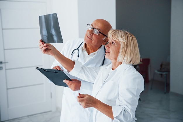 Des médecins seniors en uniforme blanc examinent les rayons X des jambes humaines.