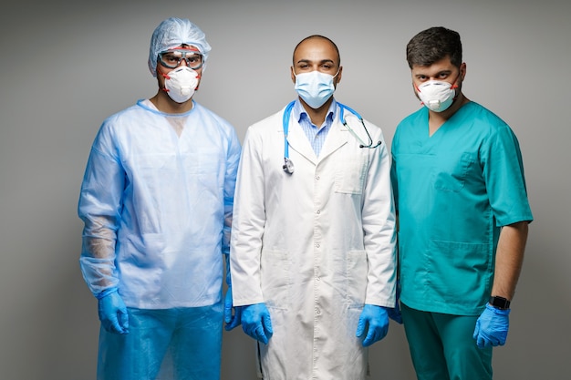 Médecins de sexe masculin en uniforme médical portant des masques debout sur fond gris, portrait