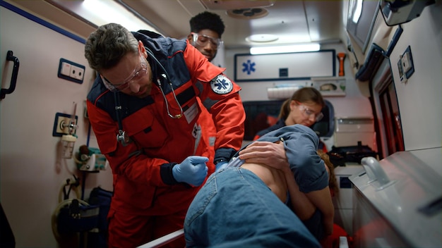 Photo des médecins d'urgence apportent les premiers soins à une victime dans une voiture d'urgence. un ambulancier multiethnique réagit rapidement pour fournir une aide médicale au patient. un assistant médical vérifie un homme de retour dans un accident de voiture.