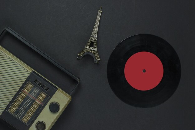 Médias rétro. Récepteur radio, disque vinyle, statuette de la Tour Eiffel sur fond noir. Vue de dessus.