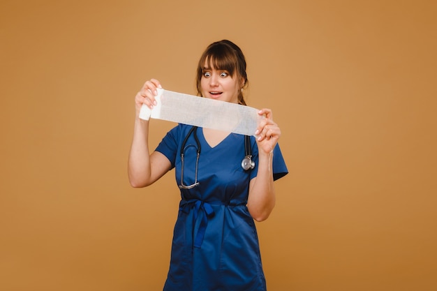 Medic femme en blouse blanche et masque tient un bandage de gaze torsadée pour panser les plaies, fond blanc