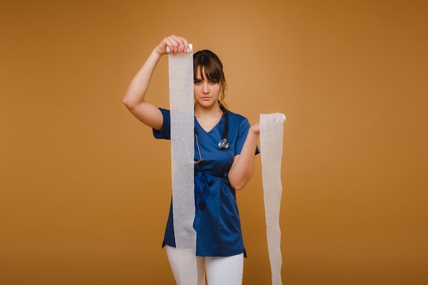 Medic femme en blouse blanche et masque tient un bandage de gaze torsadée pour panser les plaies, fond blanc