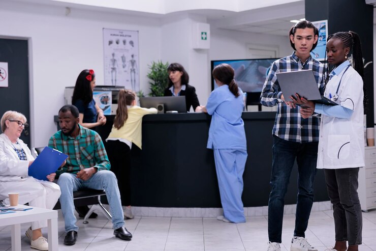 Photo medic tenant un ordinateur portable avec des résultats de laboratoire parlant avec un patient asiatique pendant qu'un médecin plus âgé admet un patient dans une clinique privée. médecin spécialiste ayant une conversation avec un jeune homme vérifiant le rendez-vous.