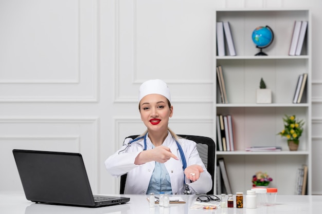 Médical beau médecin mignon en blouse blanche d'hôpital et chapeau avec ordinateur tenant des pilules blanches