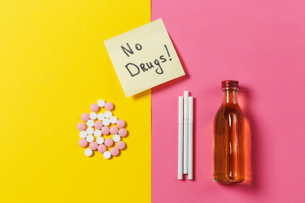 Médicaments comprimés colorés comprimés arrangés abstrait, bouteille d'alcool, cigarettes sur fond rose rose jaune