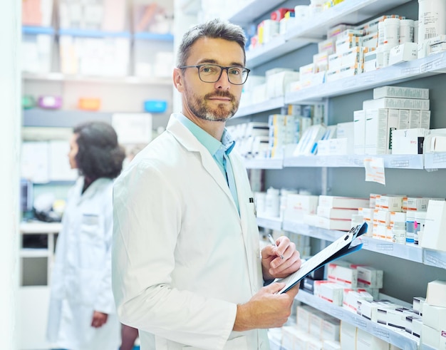 Les médicaments sont mon expertise Photo d'un homme mûr faisant l'inventaire dans une pharmacie avec son collègue en arrière-plan