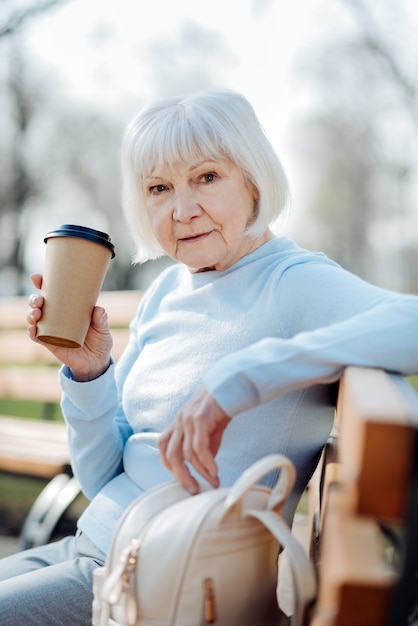 Méditatif. Femme blonde réfléchie, boire du café assis sur le banc