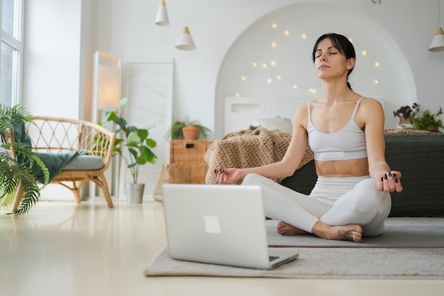 Méditation de pleine conscience de yoga en ligne femme pratiquant le yoga avec des leçons en ligne dans l'ordinateur portable à la maison femme