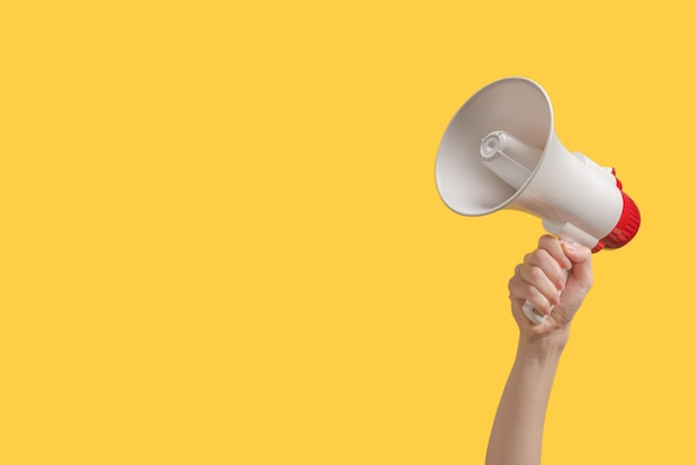 Mégaphone dans les mains de la femme sur fond jaune. Espace de copie.