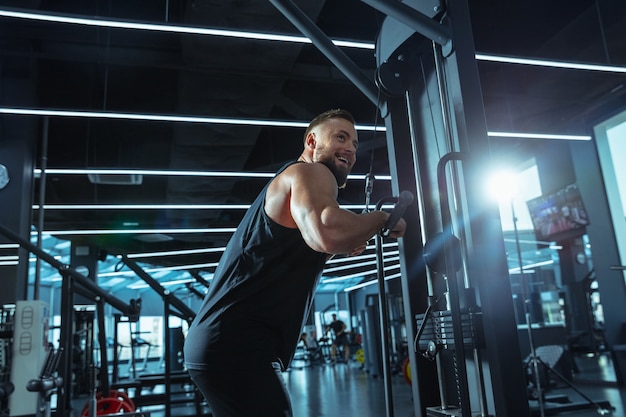 Meilleur choix. Jeune athlète caucasien musclé s'entraînant dans une salle de sport, faisant des exercices de force, pratiquant, travaillant sur le haut de son corps avec des poids et des haltères. Remise en forme, bien-être, concept de mode de vie sain.