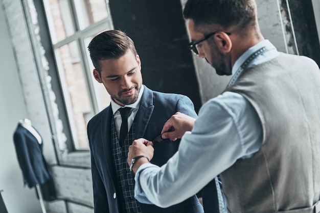 meilleur costume. jeune créateur à la mode aidant son client à s'habiller