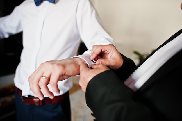 Le meilleur homme a aidé le marié élégant à porter des boutons de manchette le jour du mariage.