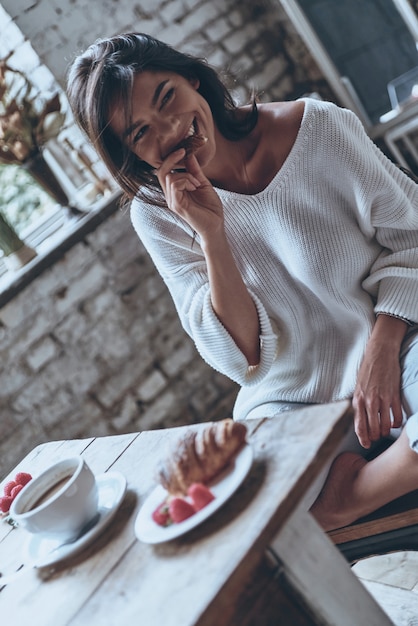 Meilleur petit déjeuner ! Jeune femme attirante regardant loin et mangeant le croissant