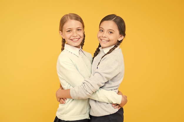 Meilleurs amis petites filles intelligentes sur fond jaune concept d'éducation retour à l'école journée de la connaissance bonheur de l'enfance mode enfant Amitié et fraternité filles heureuses en uniforme scolaire