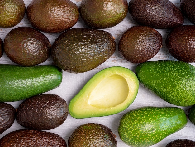 Mélange d'avocats déchirés et verts sur une planche de bois blanche.